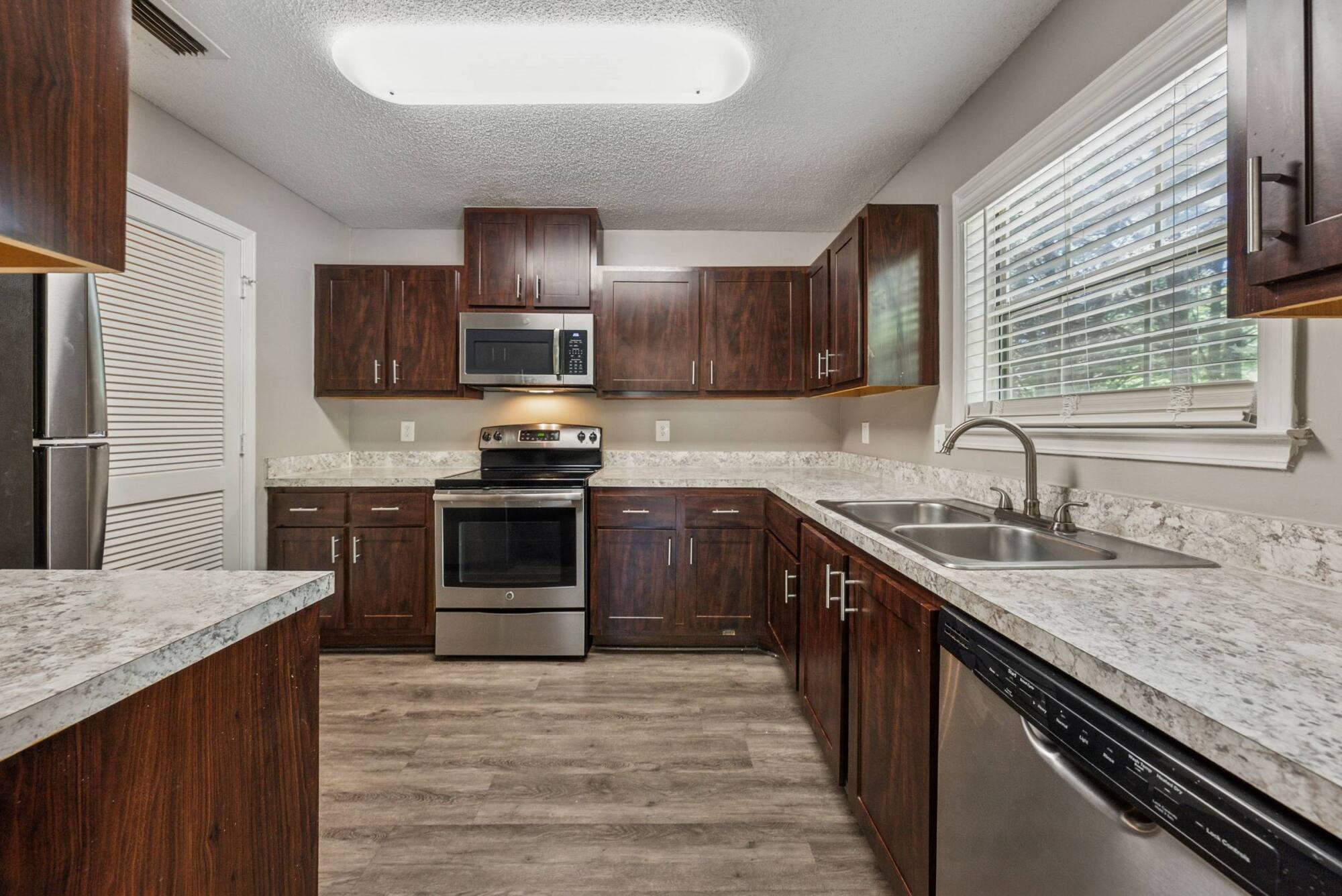 Modern kitchen with dark wood cabinets, stainless steel appliances, and light countertops and flooring.